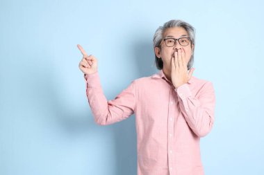 The senior Asian man standing on the blue background with pink shirt.