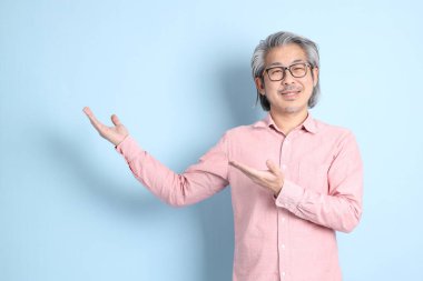 The senior Asian man standing on the blue background with pink shirt.