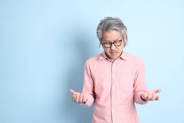 The senior Asian man standing on the blue background with pink shirt.