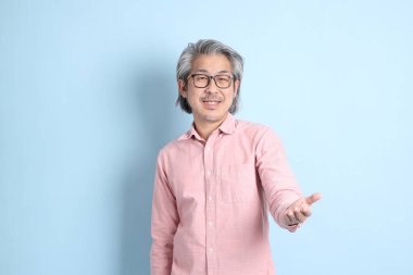 The senior Asian man standing on the blue background with pink shirt.
