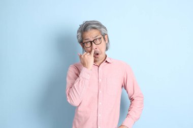 The senior Asian man standing on the blue background with pink shirt.