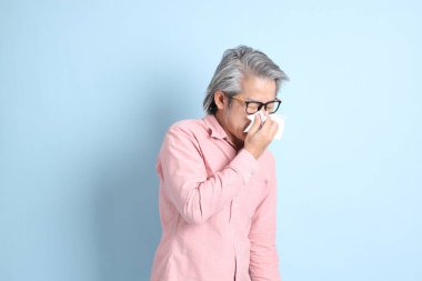 The senior Asian man standing on the blue background with pink shirt.