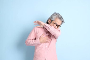 The senior Asian man standing on the blue background with pink shirt.