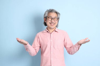 The senior Asian man standing on the blue background with pink shirt.