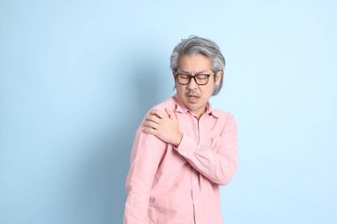 The senior Asian man standing on the blue background with pink shirt.