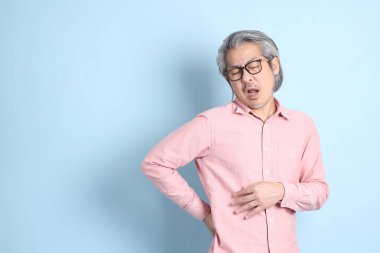 The senior Asian man standing on the blue background with pink shirt.