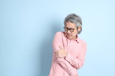 The senior Asian man standing on the blue background with pink shirt.