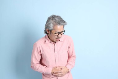 The senior Asian man standing on the blue background with pink shirt.