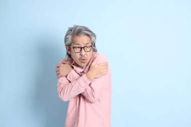 The senior Asian man standing on the blue background with pink shirt.
