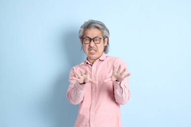 The senior Asian man standing on the blue background with pink shirt.
