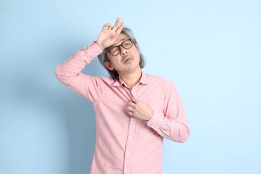 The senior Asian man standing on the blue background with pink shirt.