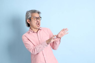 The senior Asian man standing on the blue background with pink shirt.
