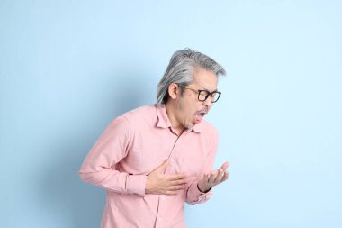 The senior Asian man standing on the blue background with pink shirt.