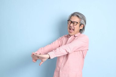 The senior Asian man standing on the blue background with pink shirt.