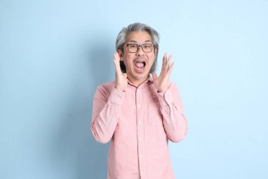 The senior Asian man standing on the blue background with pink shirt.