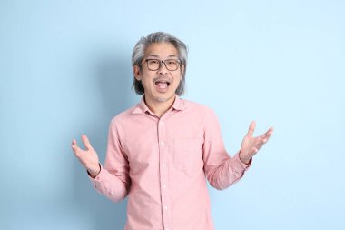 The senior Asian man standing on the blue background with pink shirt.