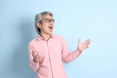 The senior Asian man standing on the blue background with pink shirt.