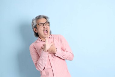 The senior Asian man standing on the blue background with pink shirt.