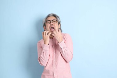 The senior Asian man standing on the blue background with pink shirt.