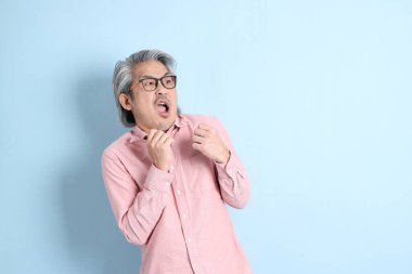 The senior Asian man standing on the blue background with pink shirt.