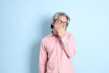 The senior Asian man standing on the blue background with pink shirt.