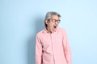 The senior Asian man standing on the blue background with pink shirt.