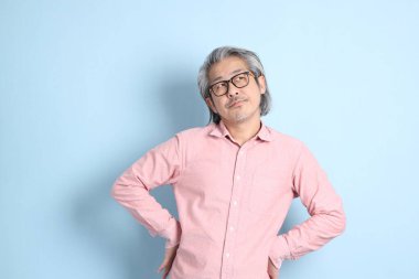 The senior Asian man standing on the blue background with pink shirt.