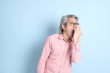 The senior Asian man standing on the blue background with pink shirt.