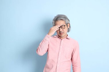 The senior Asian man standing on the blue background with pink shirt.