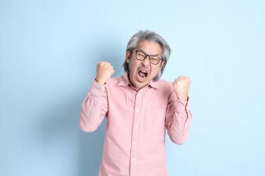 The senior Asian man standing on the blue background with pink shirt.