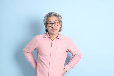 The senior Asian man standing on the blue background with pink shirt.