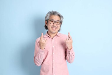 The senior Asian man standing on the blue background with pink shirt.