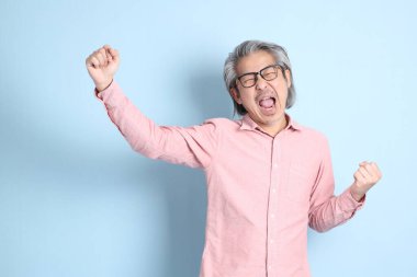 The senior Asian man standing on the blue background with pink shirt.