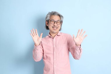 The senior Asian man standing on the blue background with pink shirt.
