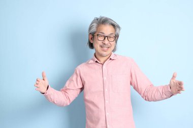 The senior Asian man standing on the blue background with pink shirt.