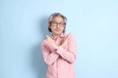 The senior Asian man standing on the blue background with pink shirt.