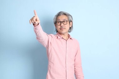 The senior Asian man standing on the blue background with pink shirt.