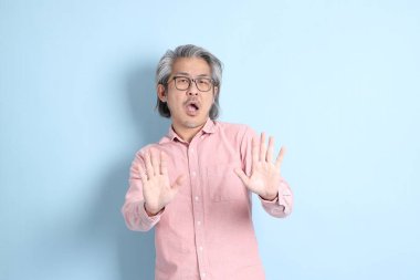 The senior Asian man standing on the blue background with pink shirt.