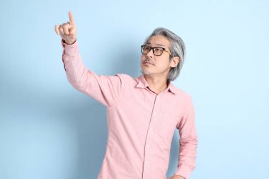 The senior Asian man standing on the blue background with pink shirt.