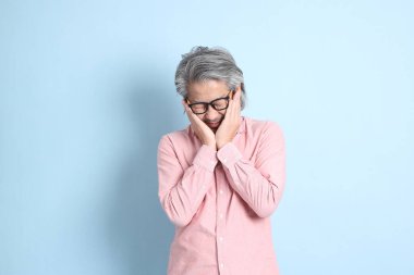 The senior Asian man standing on the blue background with pink shirt.