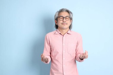 The senior Asian man standing on the blue background with pink shirt.