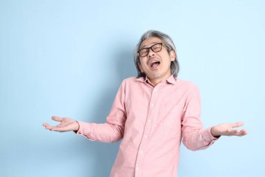 The senior Asian man standing on the blue background with pink shirt.