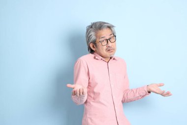 The senior Asian man standing on the blue background with pink shirt.