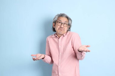 The senior Asian man standing on the blue background with pink shirt.