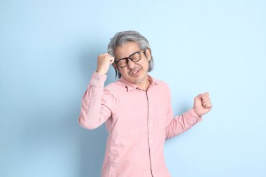 The senior Asian man standing on the blue background with pink shirt.