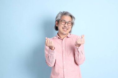 The senior Asian man standing on the blue background with pink shirt.