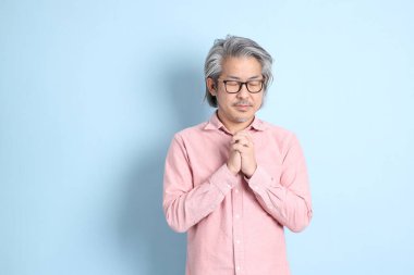 The senior Asian man standing on the blue background with pink shirt.