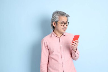 The senior Asian man standing on the blue background with pink shirt.