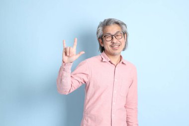 The senior Asian man standing on the blue background with pink shirt.