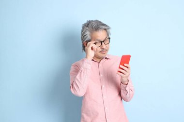 The senior Asian man standing on the blue background with pink shirt.